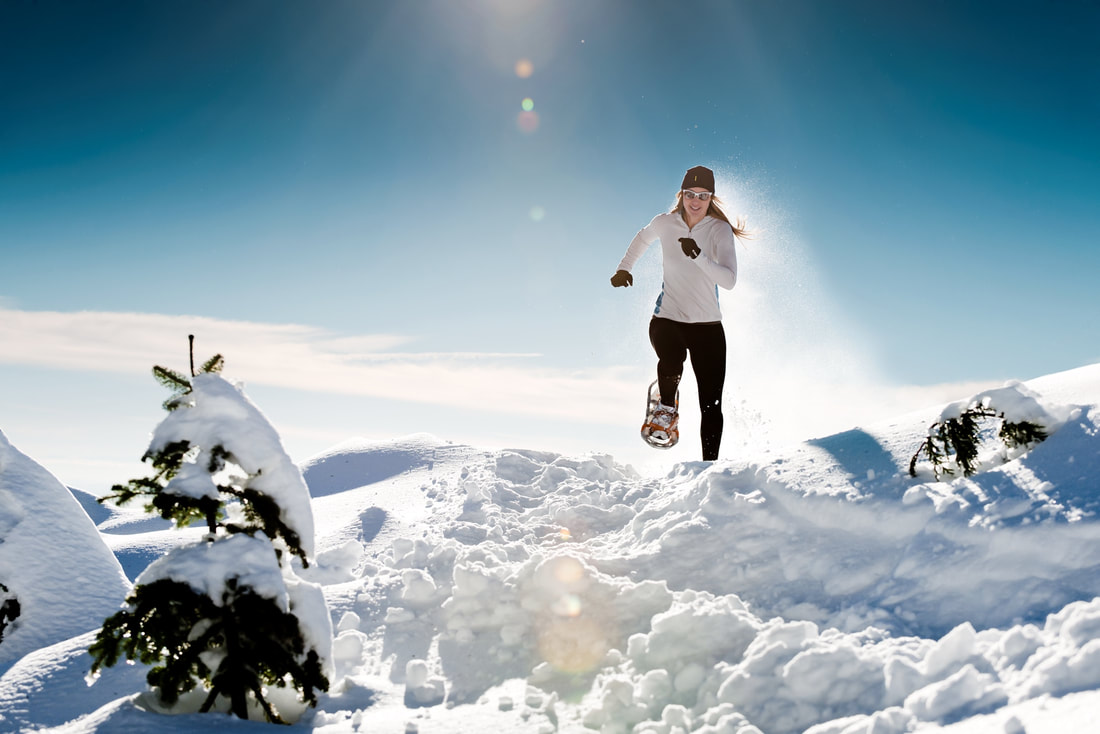 Athletic woman running through deep snow with snowshoes on a sunny day.